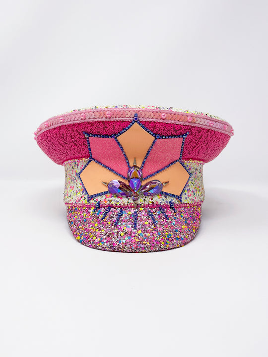 Festival captain hat with pink sequins, colourful glitter peak, Jukebox logo jewel detail, and glow-in-the-dark reflective starburst design – perfect for rave, costume, or party wear.
