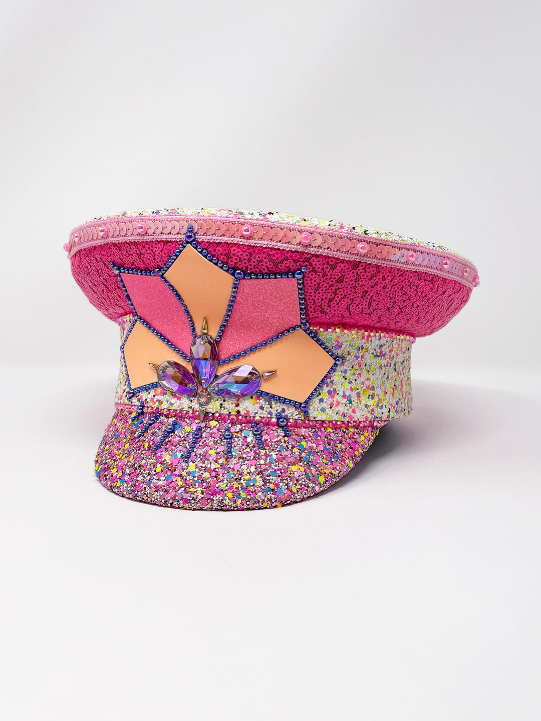 Festival captain hat with pink sequins, colourful glitter peak, Jukebox logo jewel detail, and glow-in-the-dark reflective starburst design – perfect for rave, costume, or party wear.
